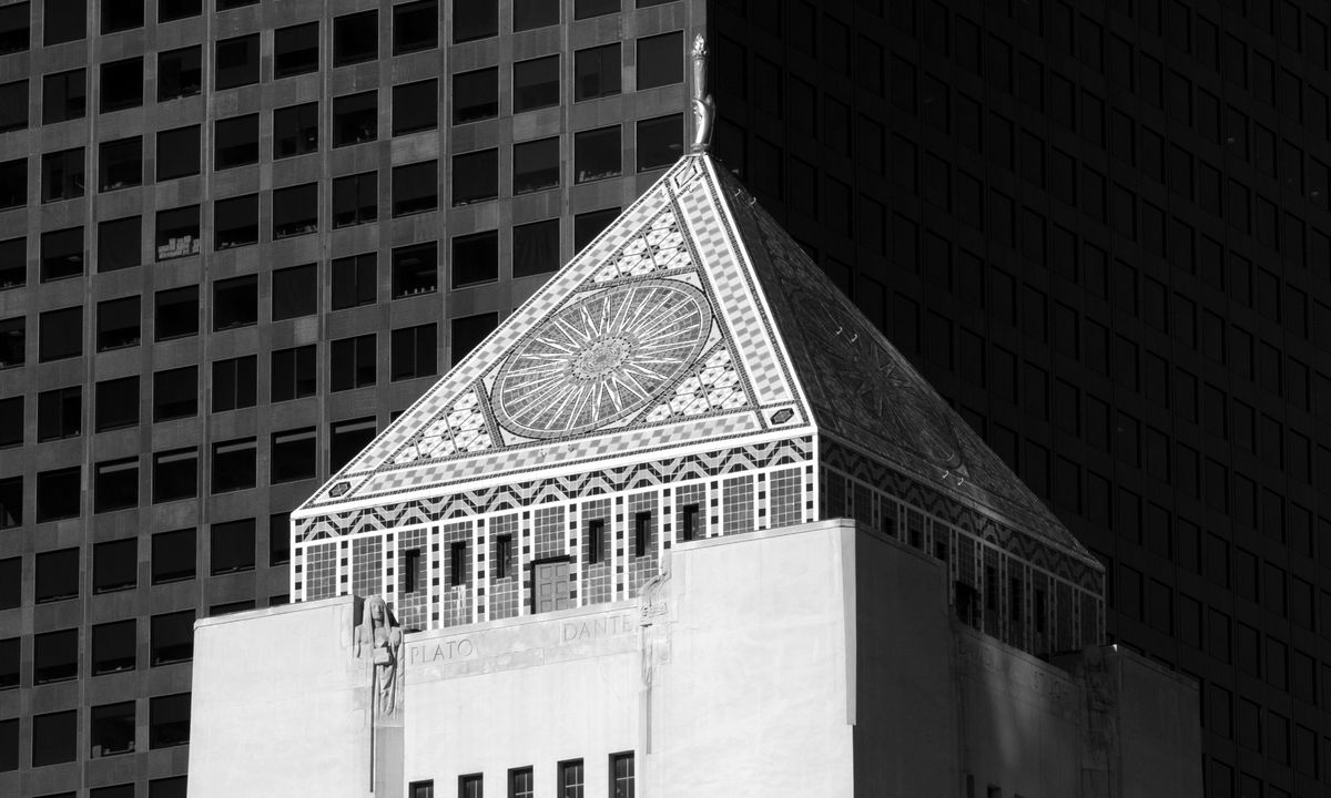 Black-and-white photograph of the stepped tower and tiled pyramid of the Los Angeles Central Library against a dark glass skyscraper